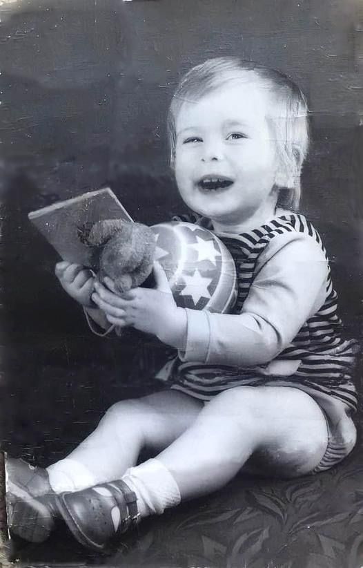 A black and white vintage photo of a smiling toddler in striped clothing holding a toy.