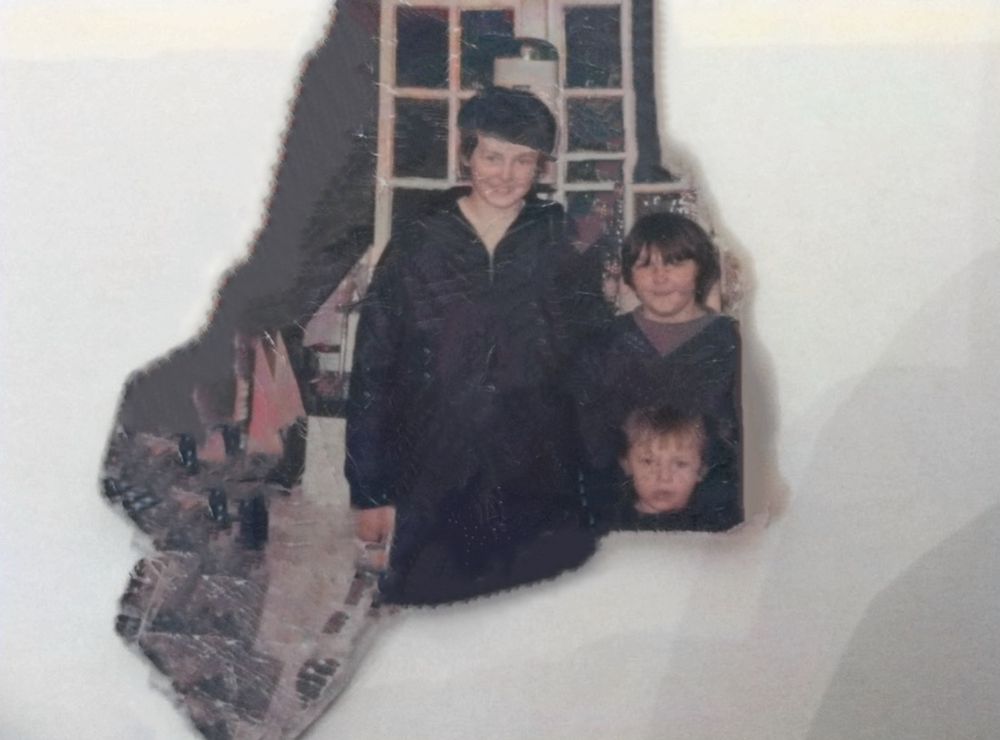 A torn vintage photograph showing three people standing together indoors.