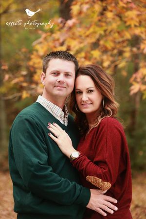 Romantic couple in coordinating sweaters against autumn foliage backdrop.