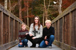 Family portrait on wooden bridge with autumn colors in background.