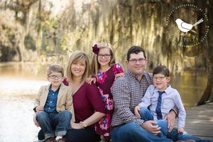 Family sitting together on wooden dock near water with Spanish moss in background.