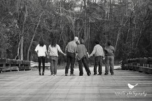 Black and white photo of people walking together on wooden boardwalk through nature.