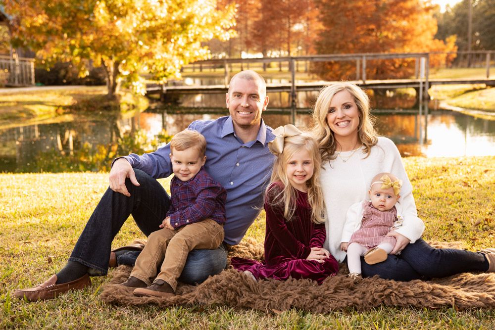 Family group portrait outdoors near pond with autumn colors in background.