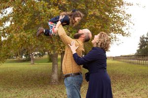 Family enjoying playtime together beneath autumn trees in park setting.