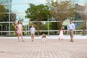 Family spread out in playful poses on urban plaza with modern building behind them.