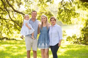 A family poses together on a sunny day outdoors with trees and natural lighting in the background.