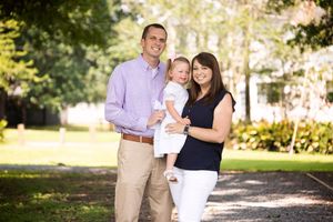 A family stands together on a path in a sunlit park setting.