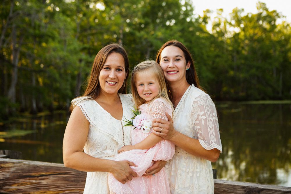 Three people pose together on a wooden deck overlooking a serene lake at sunset.