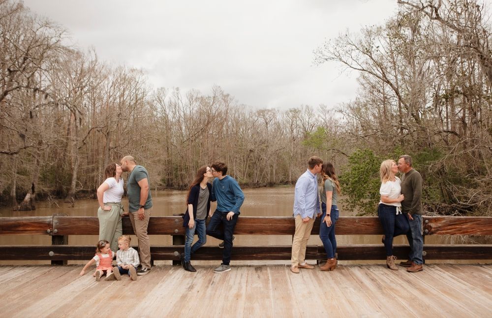Multiple couples lean against a wooden railing during an outdoor group photoshoot.