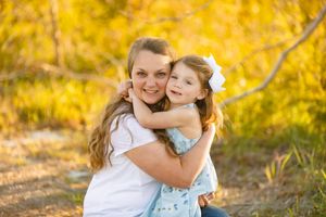 Parent and child share a joyful embrace outdoors against a golden autumn background.