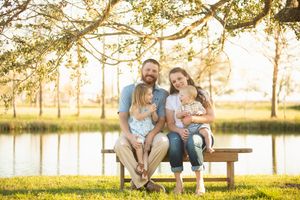 Family of four sits together on wooden bench by lake during golden hour.