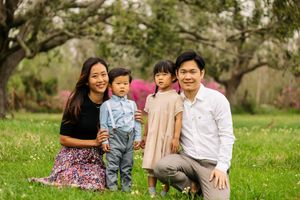 Family of four poses together in blooming spring garden with trees in background.