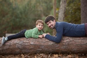Parent and child lying together on fallen log in autumn forest setting.