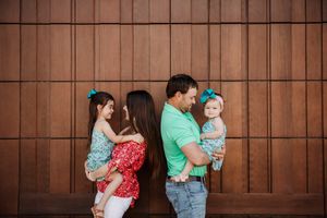 Two couples with small children pose against a wooden wall background.