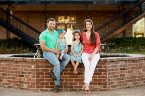 A family sits together on brick steps in front of an industrial-style building.