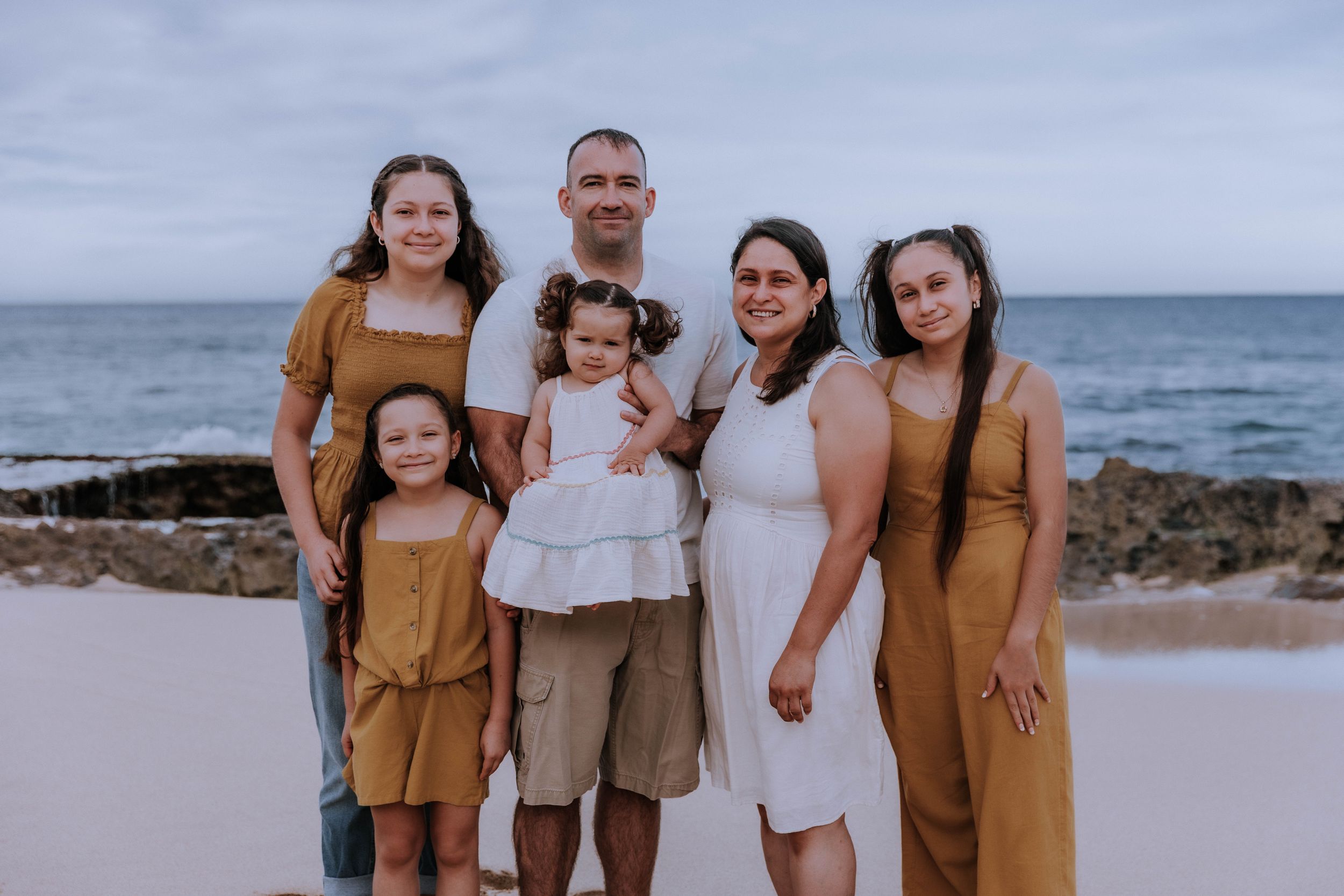 A family portrait on the beach with everyone wearing coordinated earth-tone outfits.