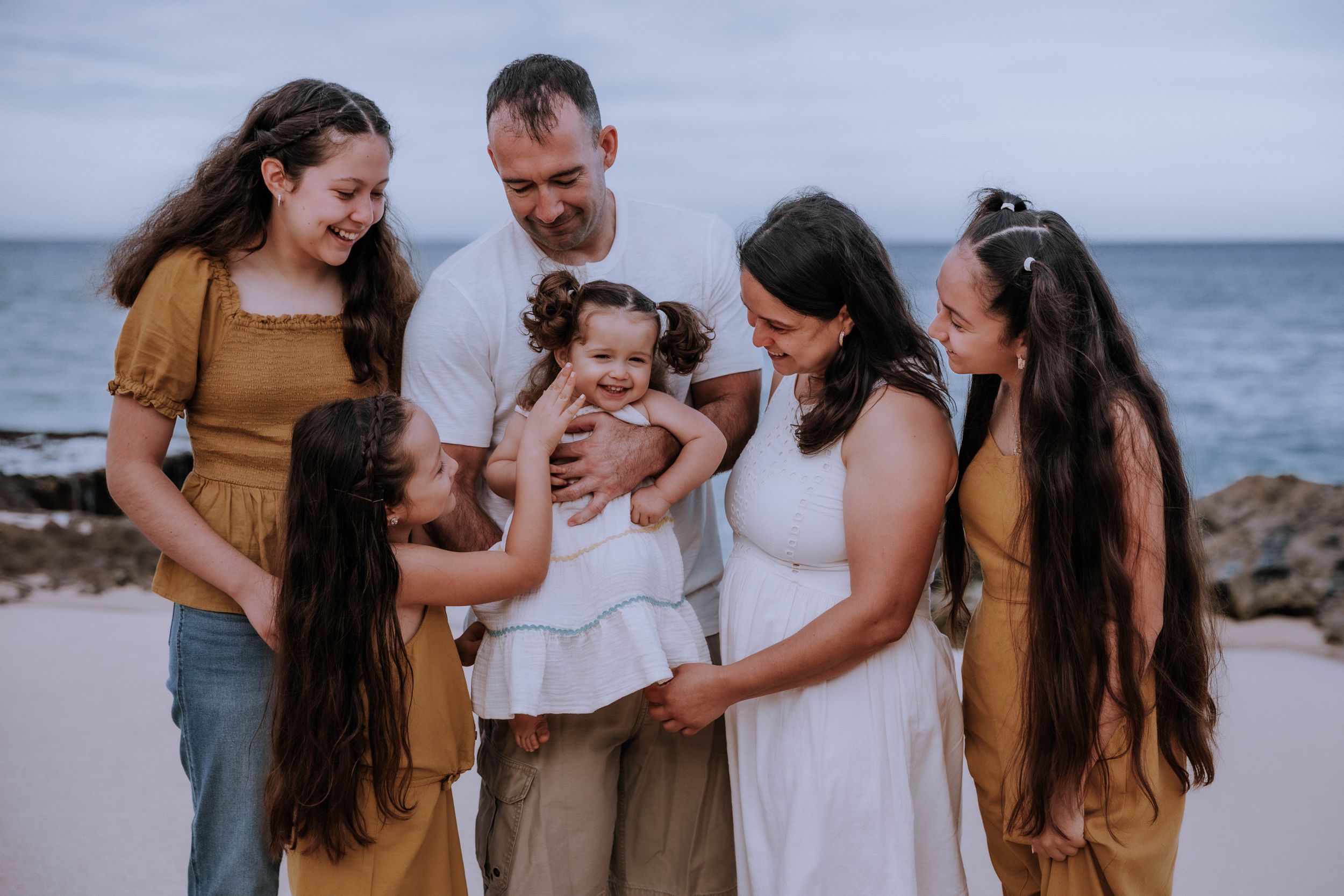 A casual beach family photo with everyone dressed in complementary brown and white tones.