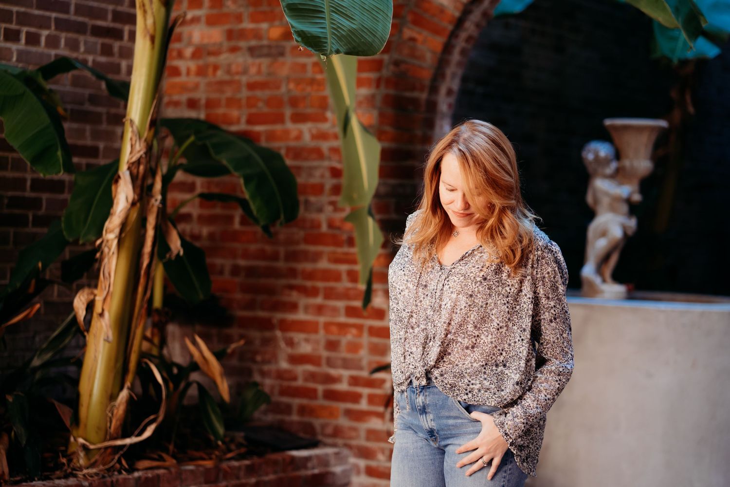 Casual portrait against brick wall with tropical plants and natural lighting.