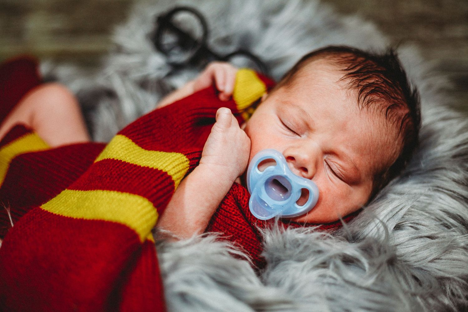 Newborn baby sleeping peacefully on grey fur with red and yellow blanket.