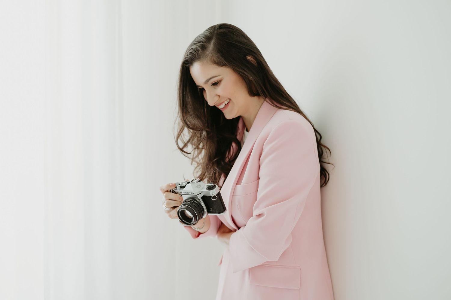 Professional photographer in pink blazer examining vintage camera against white background.
