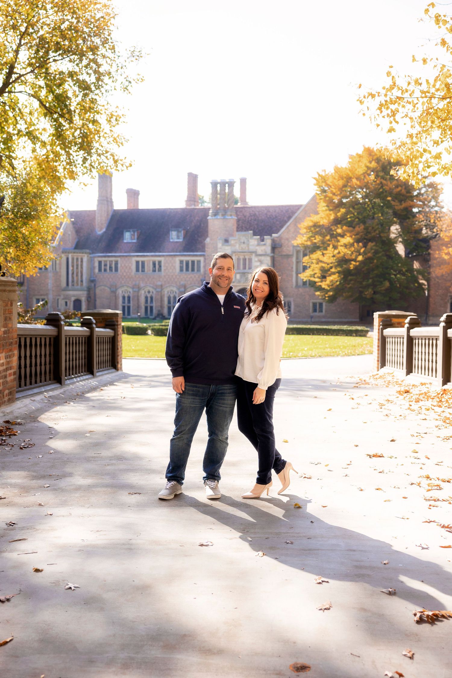 Couple walking together on pathway with grand estate building visible in autumn background.