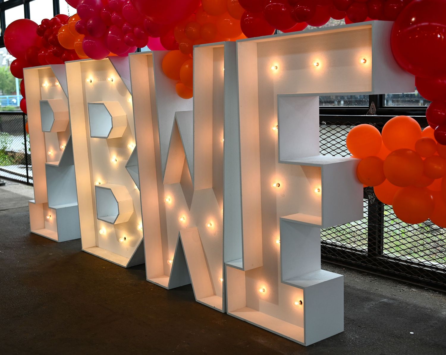 Illuminated white BWIE marquee letters with red balloon decorations.