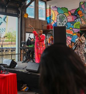 Performer in red dress on stage at indoor venue with vibrant graffiti-style backdrop.