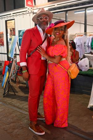 A stylish couple in coordinating red and coral outfits poses at an outdoor market.