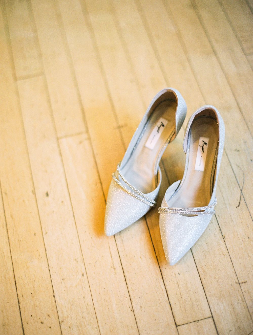 Silver pointed toe bridal shoes on wooden flooring.