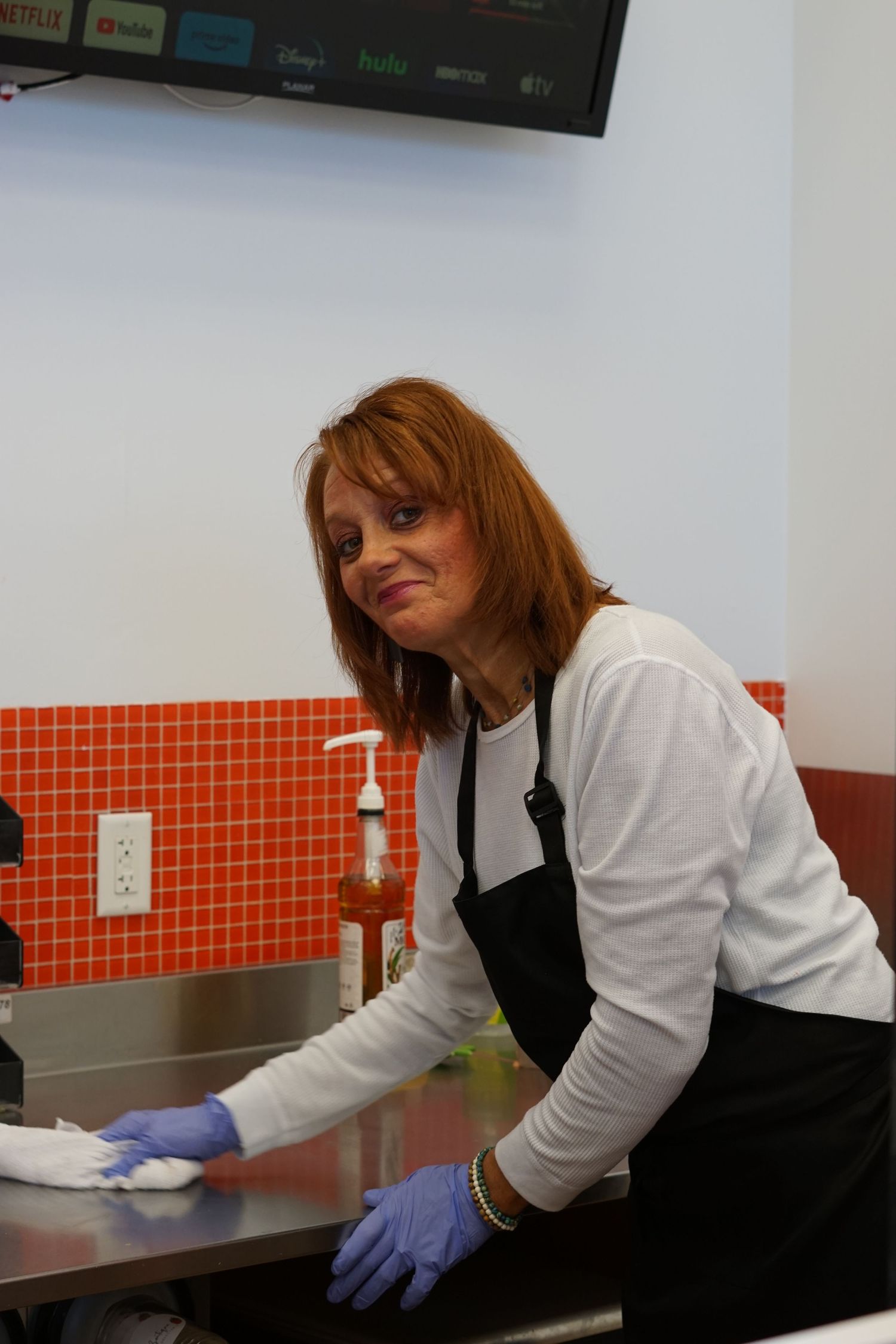 Female worker in apron and gloves cleaning stainless steel counter in a modern kitchen.