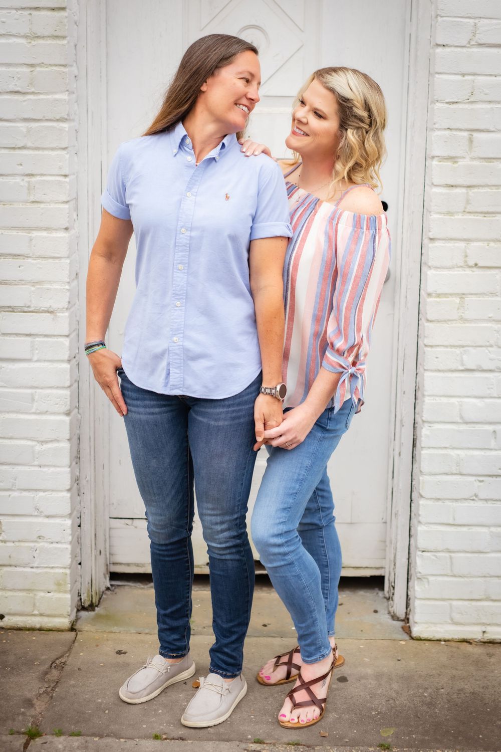 A couple in casual attire sharing a joyful moment against a white brick wall.