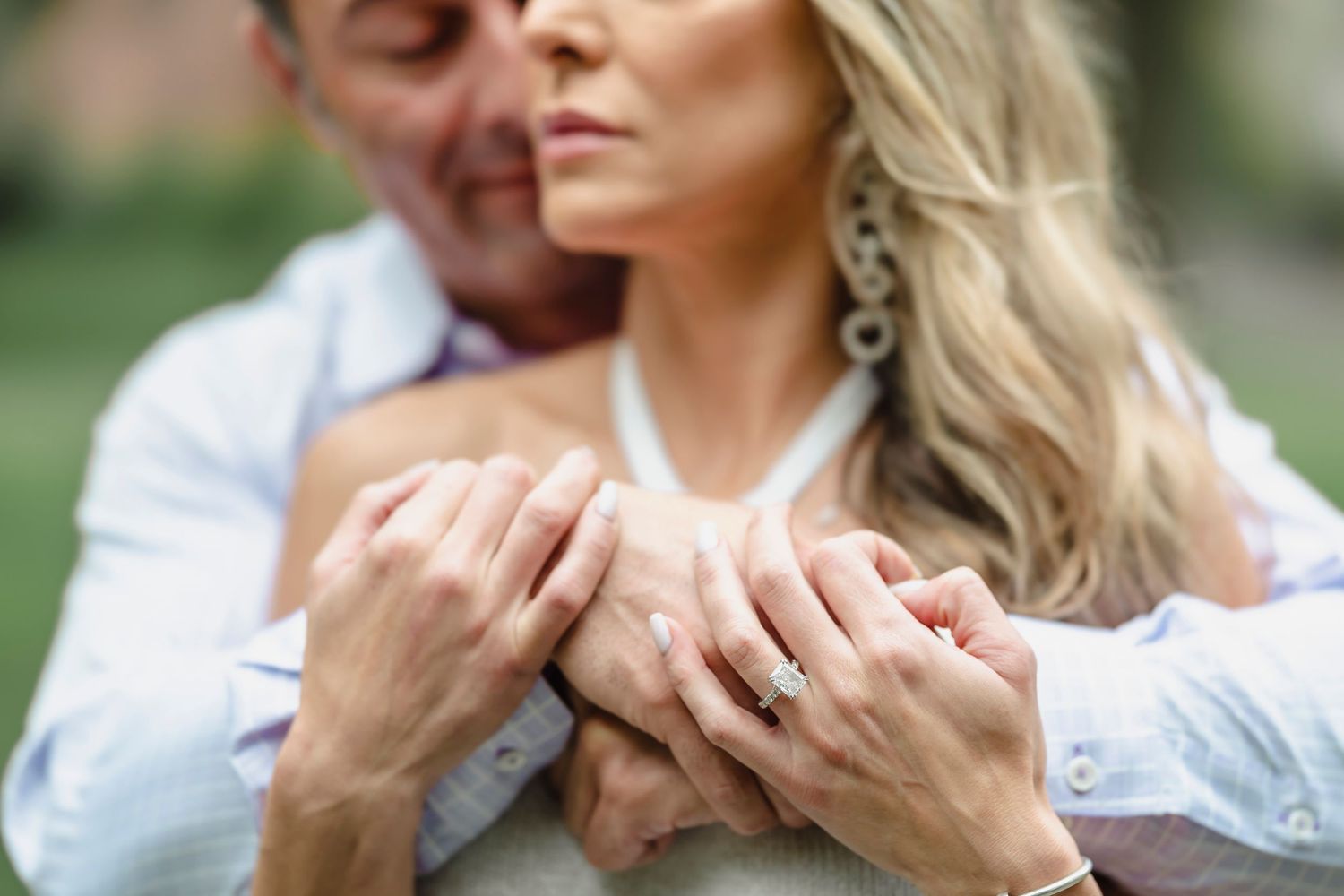 Detail shot of hands with engagement ring in natural outdoor setting.