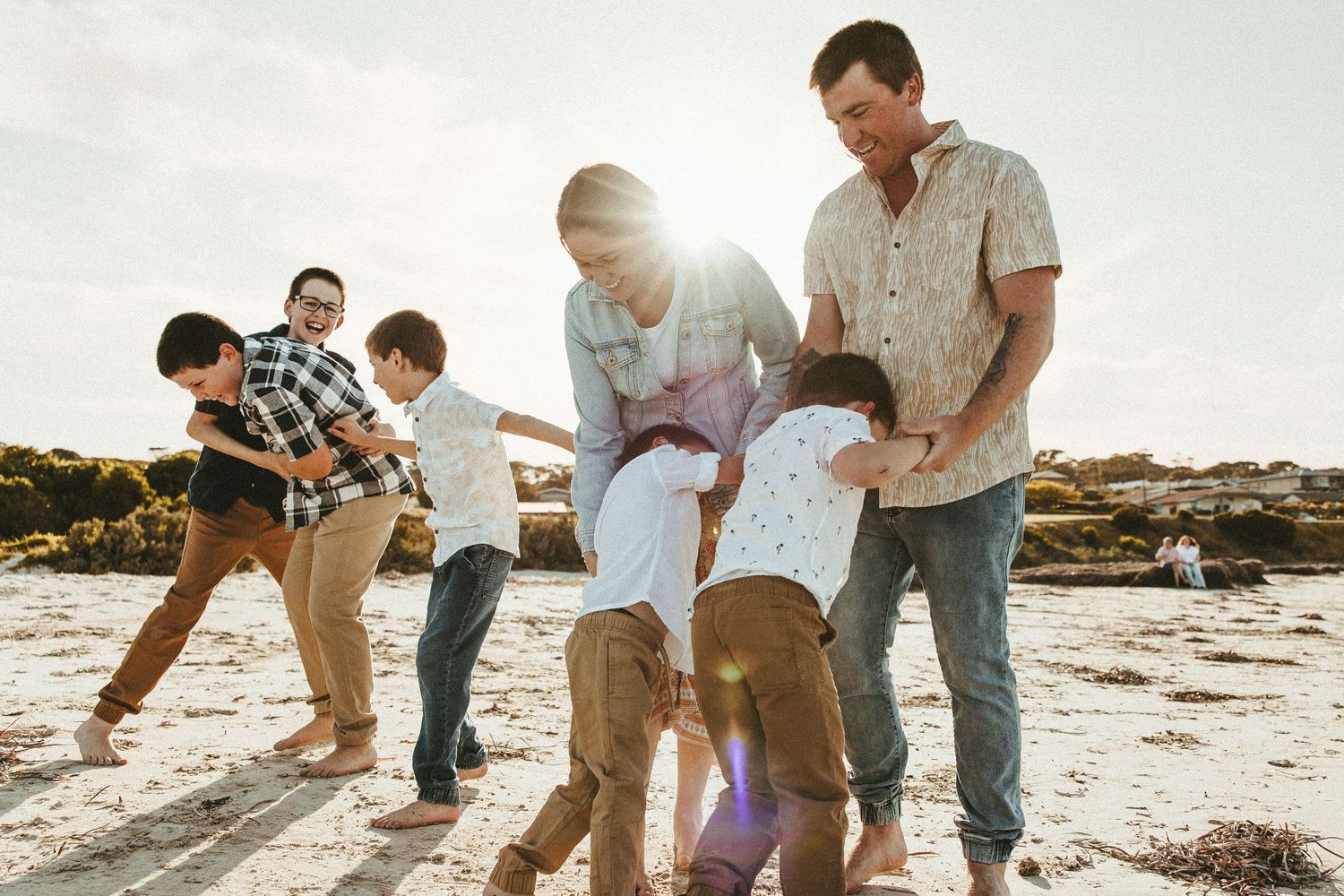 Family playing together on sandy beach during golden hour with children running and laughing.