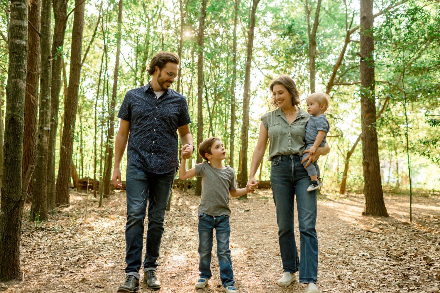 Family walking and playing together in a wooded forest setting on a sunny day.