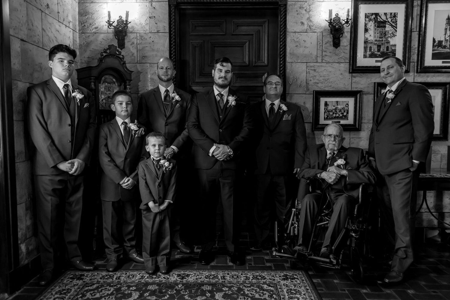 Formal group portrait in black and white against stone wall with vintage decor.