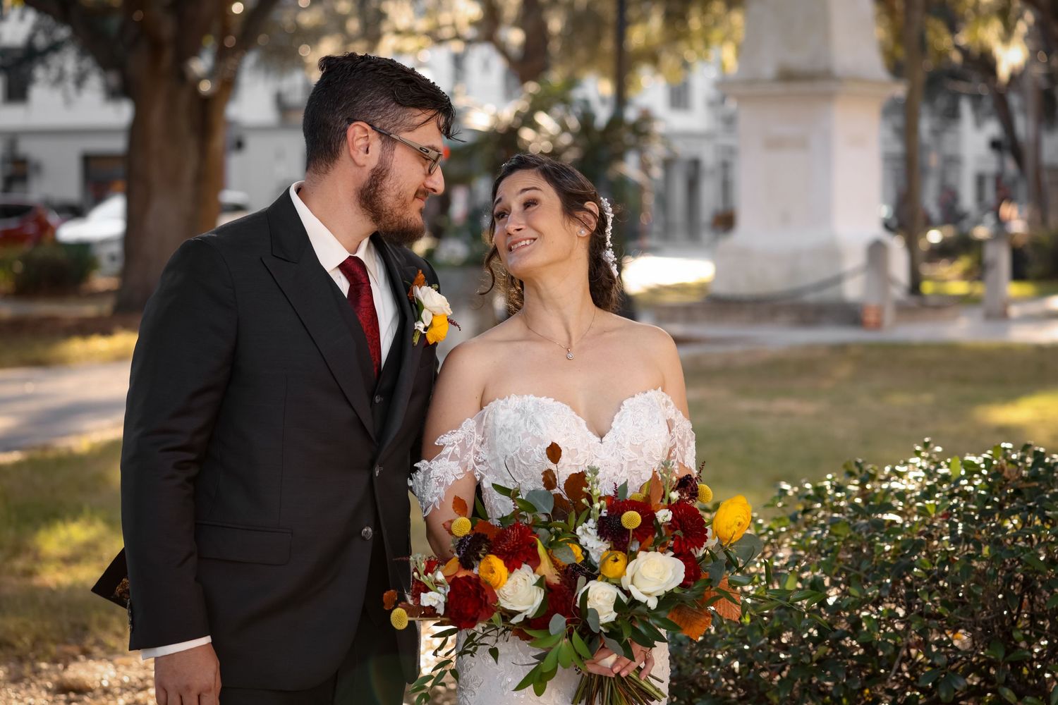 Couple posing outdoors with autumn floral bouquet featuring deep red blooms.