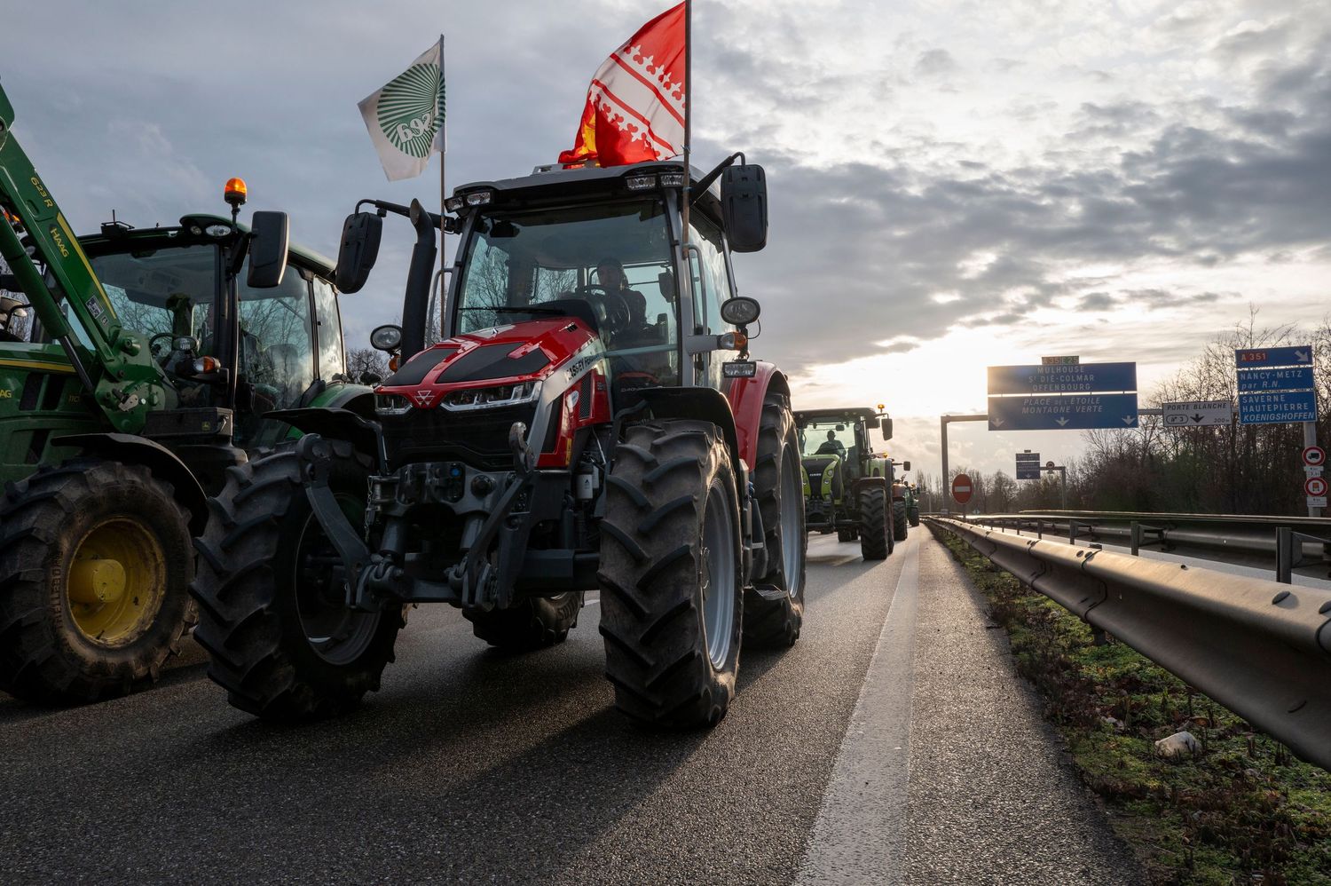 Large tractors with flags line up during a protest on a highway at dusk.