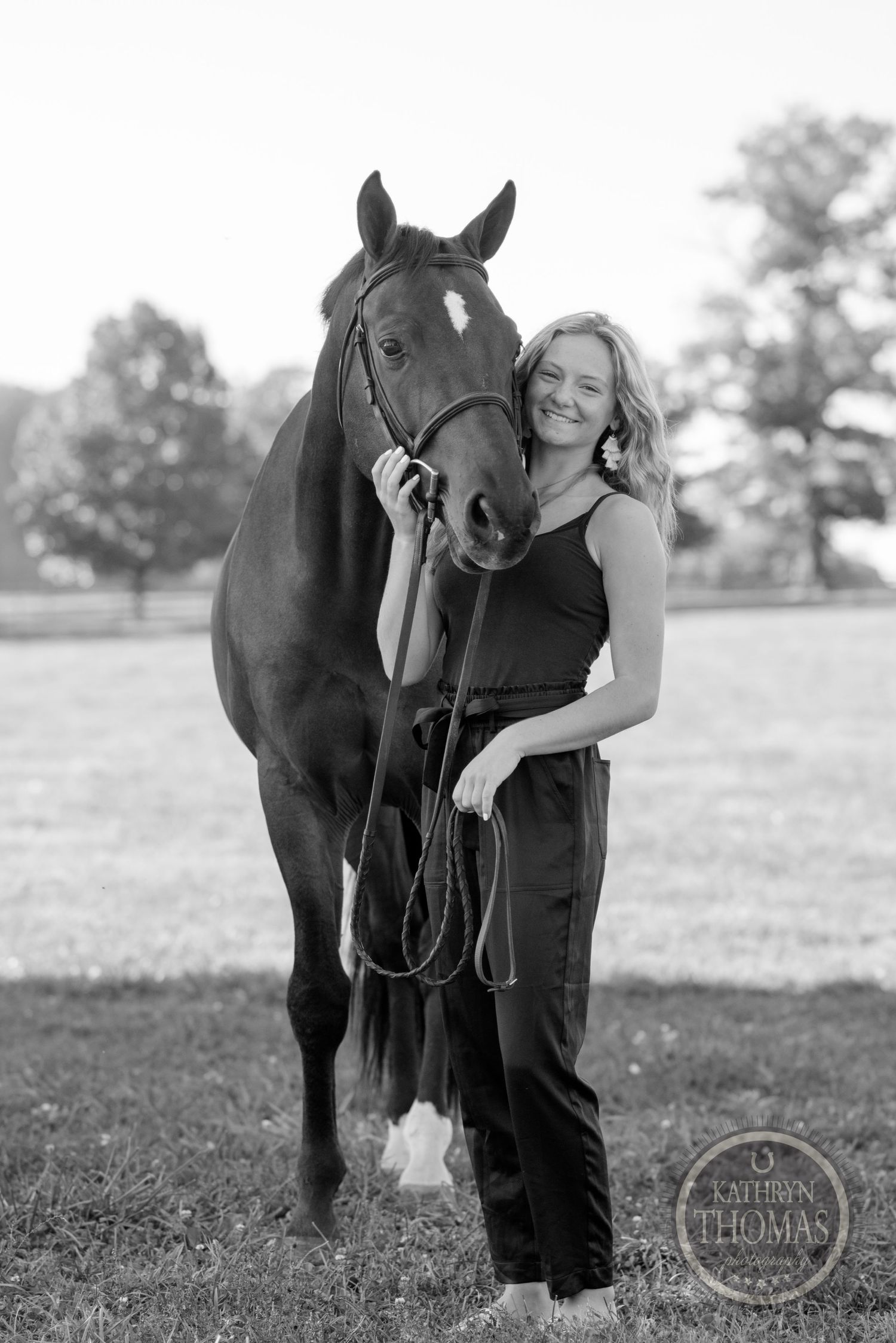 A black-clad equestrian poses with a beautiful bay horse in a pastoral setting.