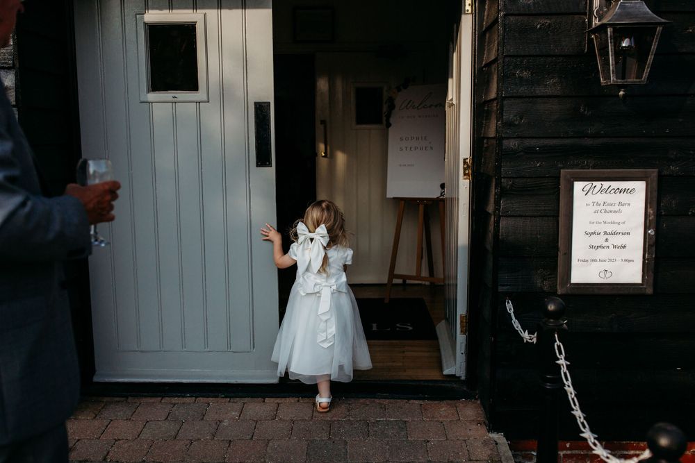 A child in a white dress peeks out from behind a gray door at an event venue.