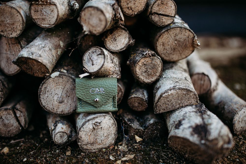 Green velvet ring box placed artistically on stack of rustic wooden logs.
