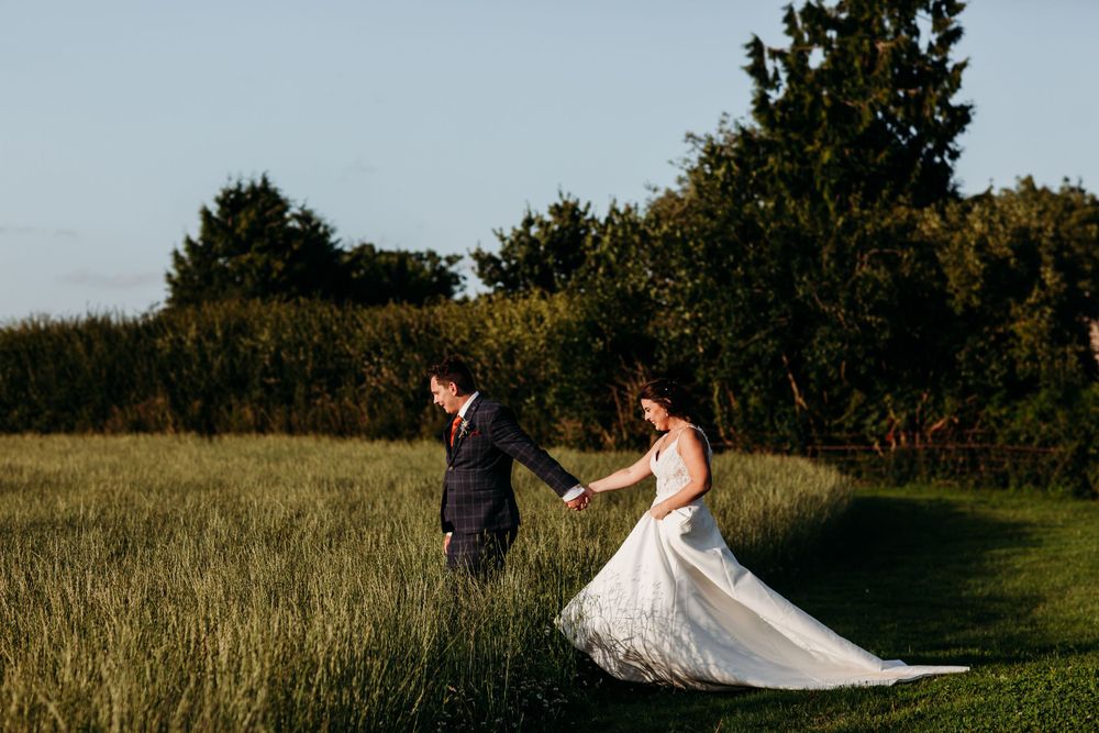 A couple enjoys a playful moment in a sunlit field during their wedding photoshoot.