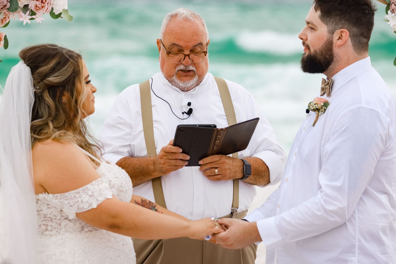 A beach wedding ceremony being conducted with turquoise ocean waves in background.