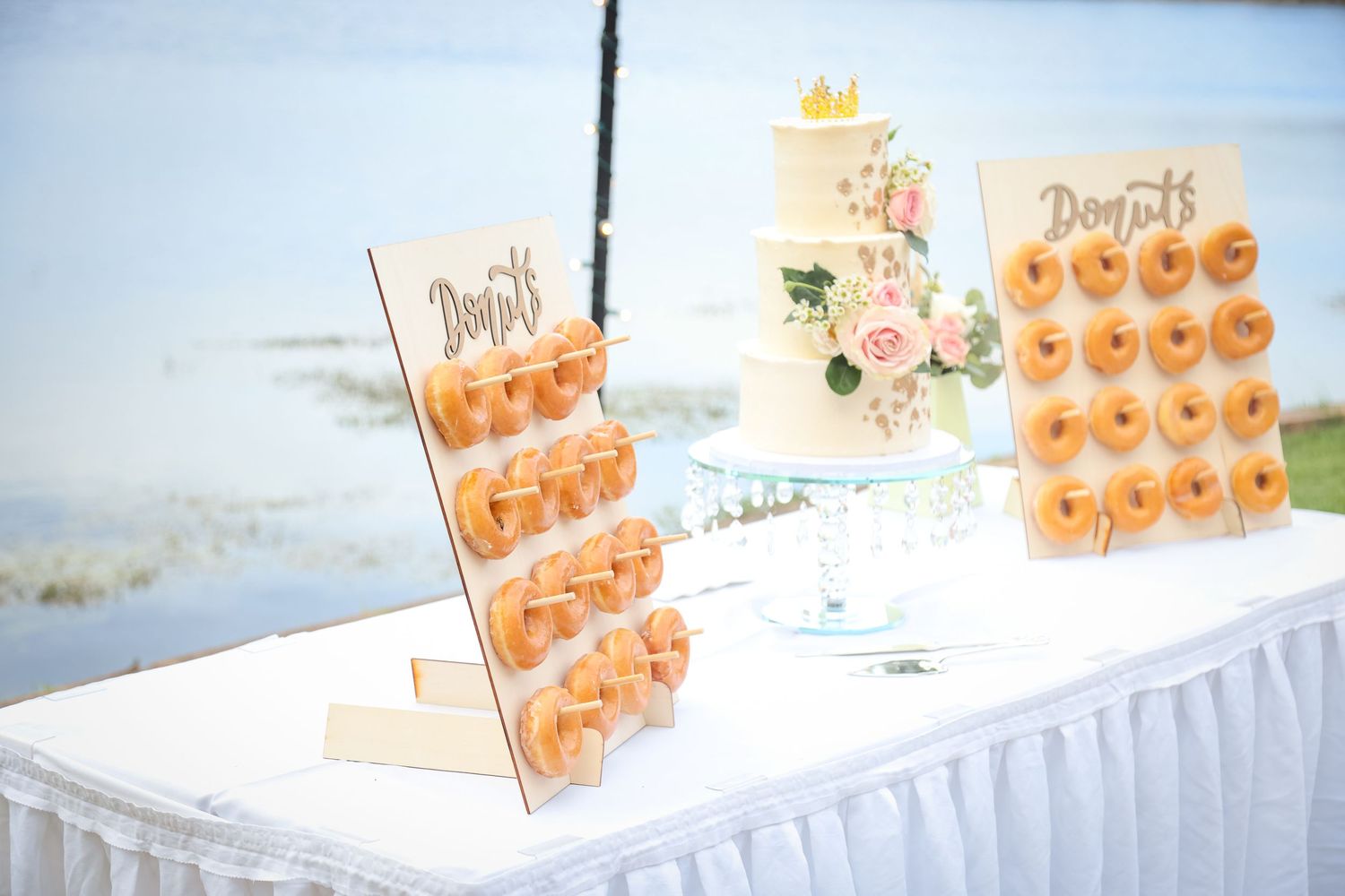Wedding display features tiered donut stands and a floral decorated cake on a white tablecloth.