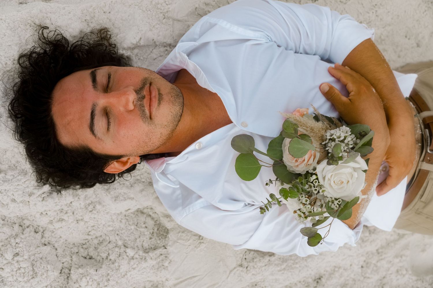 A bouquet of white roses and eucalyptus rests on a reclining figure wearing a light blue shirt.