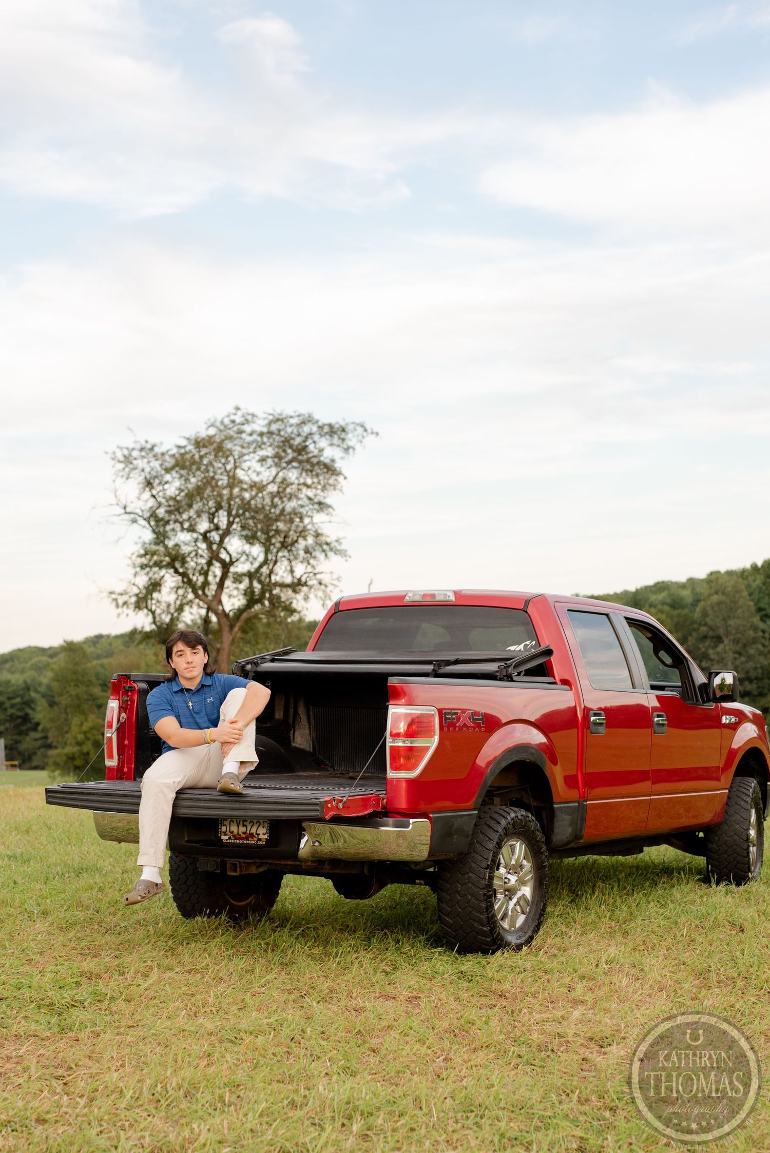 A red Ford F150 pickup truck parked in a grassy field with someone sitting on the open tailgate.