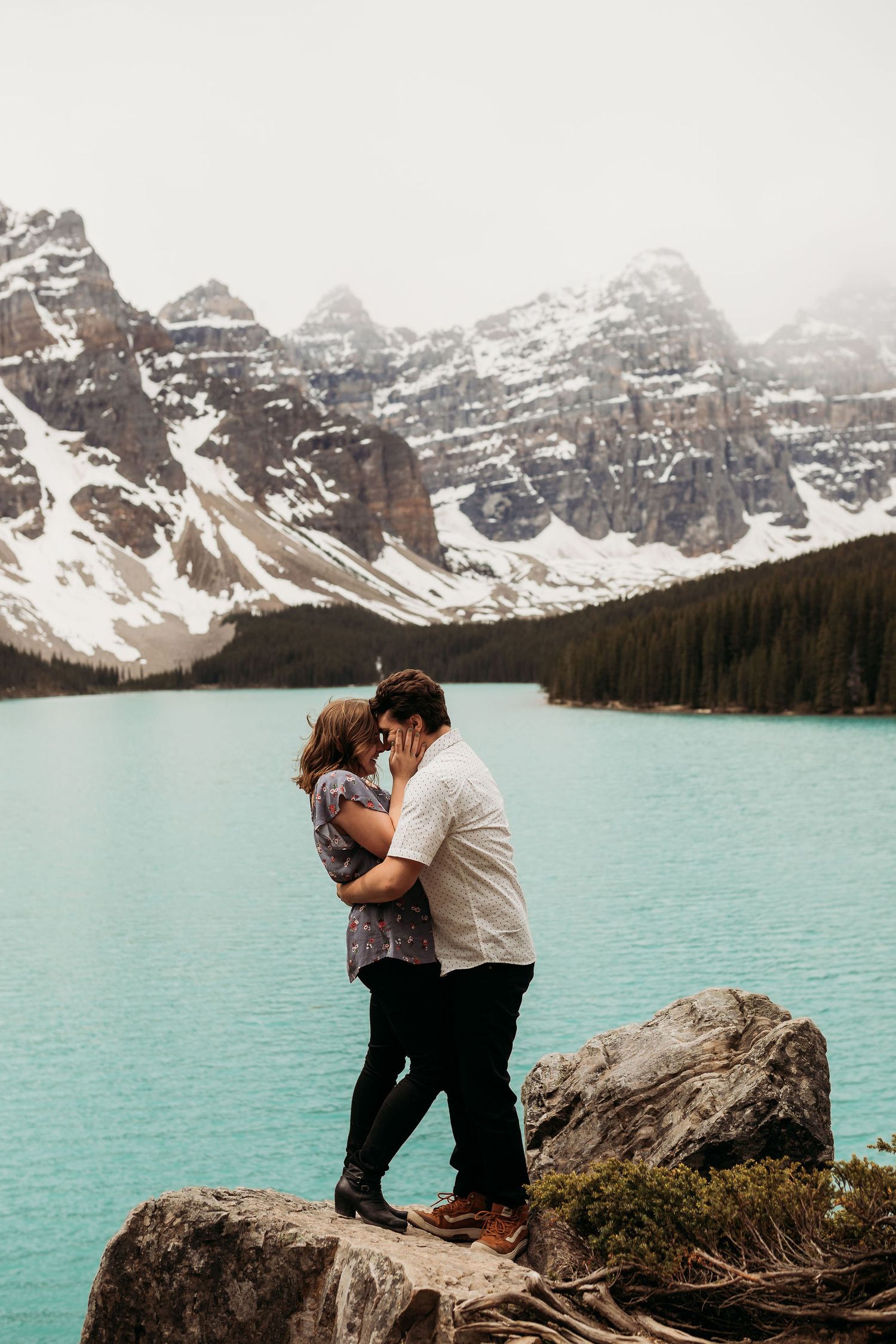 Intimate moment between couple on rocky outcrop overlooking turquoise alpine lake.