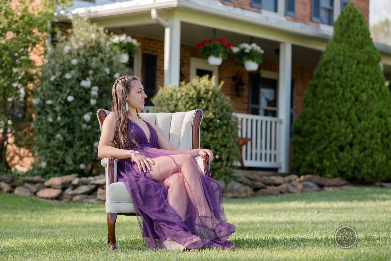 Woman in flowing purple dress lounges elegantly on outdoor chair near garden porch.