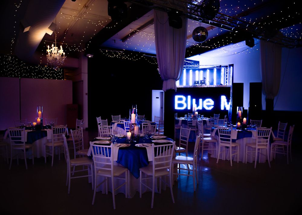 Elegant event space with blue lighting, white chairs, and round tables set for a special occasion.