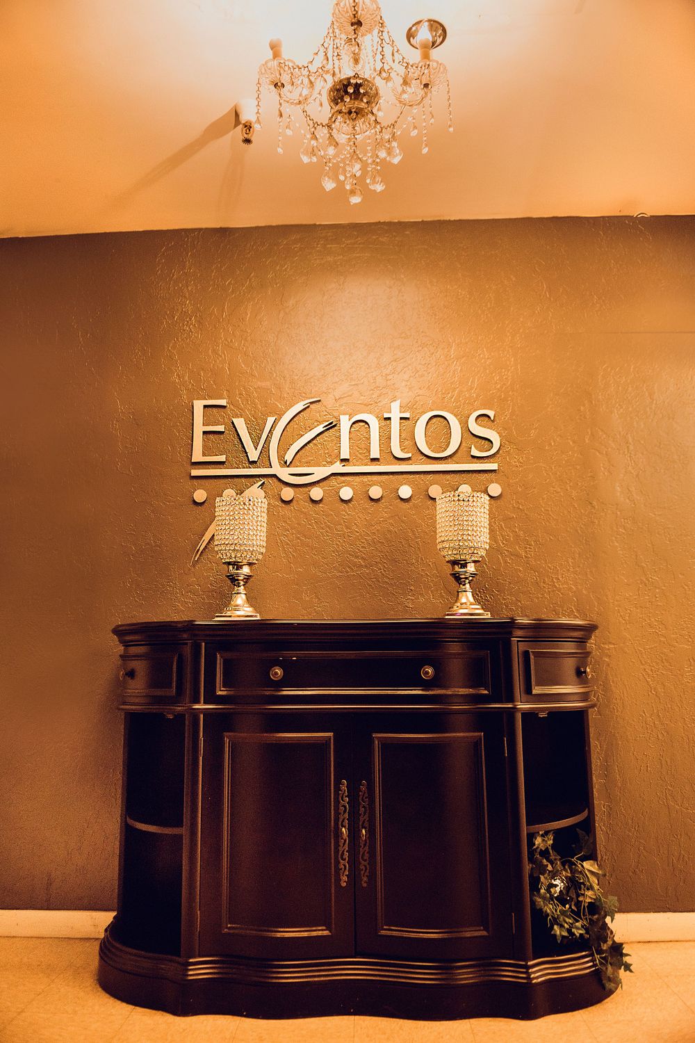 Elegant entryway featuring an ornate chandelier, vintage cabinet, and 'Eventos' signage on the wall.