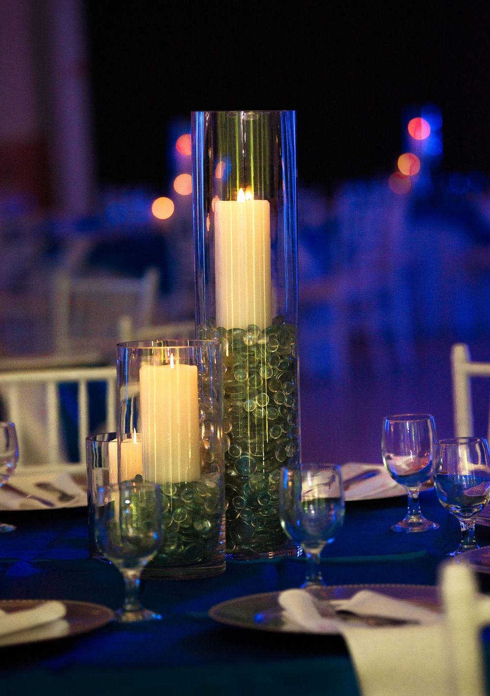 Elegant table setting with tall glass cylinder candle centerpieces and blue ambient lighting.